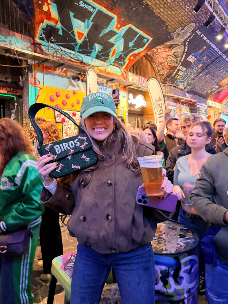 Phannies customer smiling and holding green BIRDS beaded bag at bar